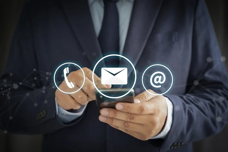A person holding a phone beside illustrated telephone, envelope and at-sign icons, representing ways to make contact.