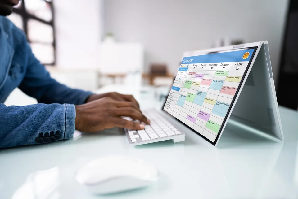 A person at a desk working through a weekly calendar on a laptop screen.
