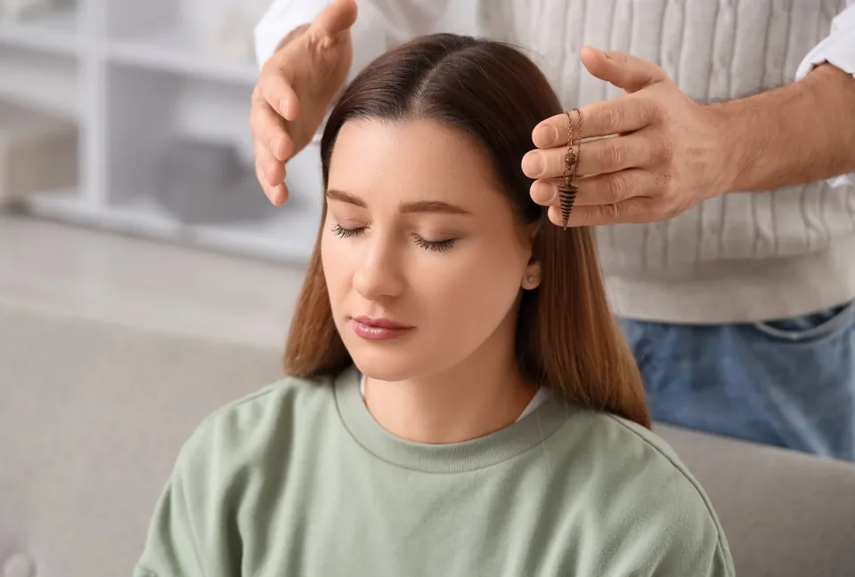 A seated client rests with her eyes closed while a practitioner guides a session with a gentle hand gesture nearby.